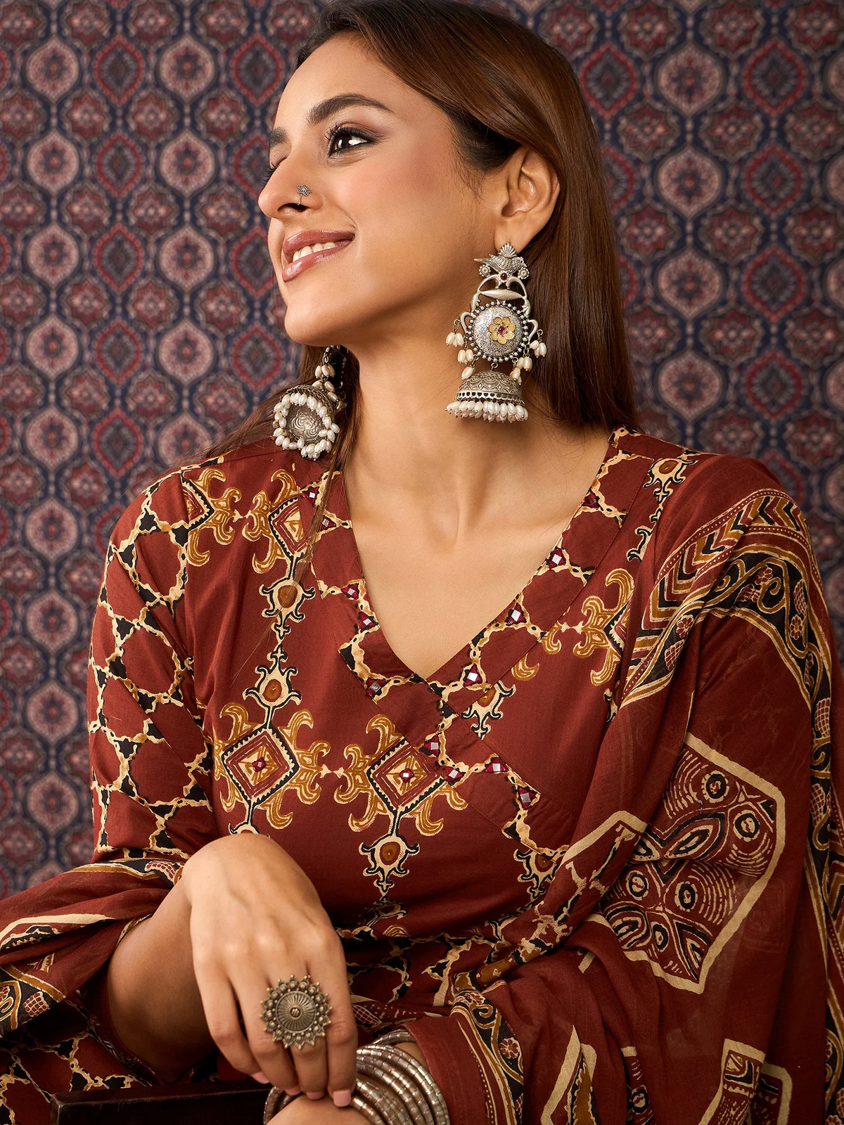 Woman wearing a patterned dress with jewelry against a decorative background