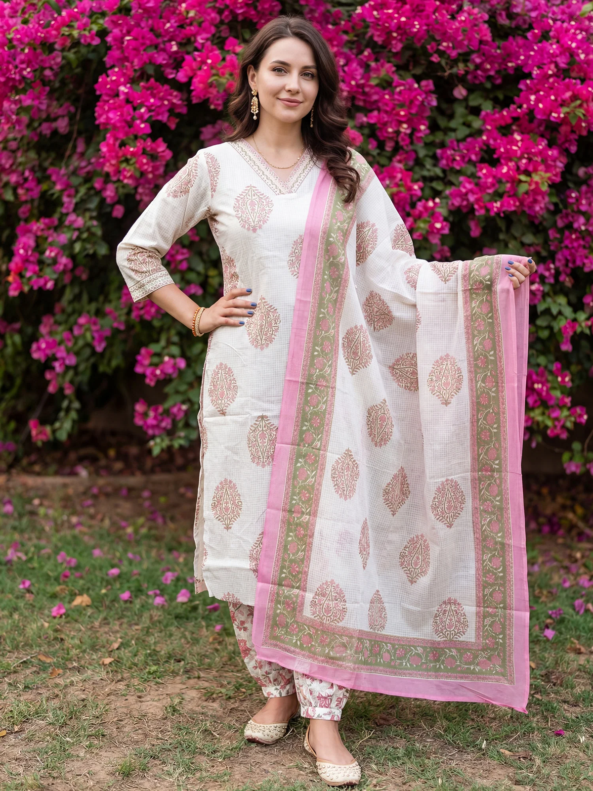Woman in a traditional outfit with a pink dupatta standing in front of pink flowers.