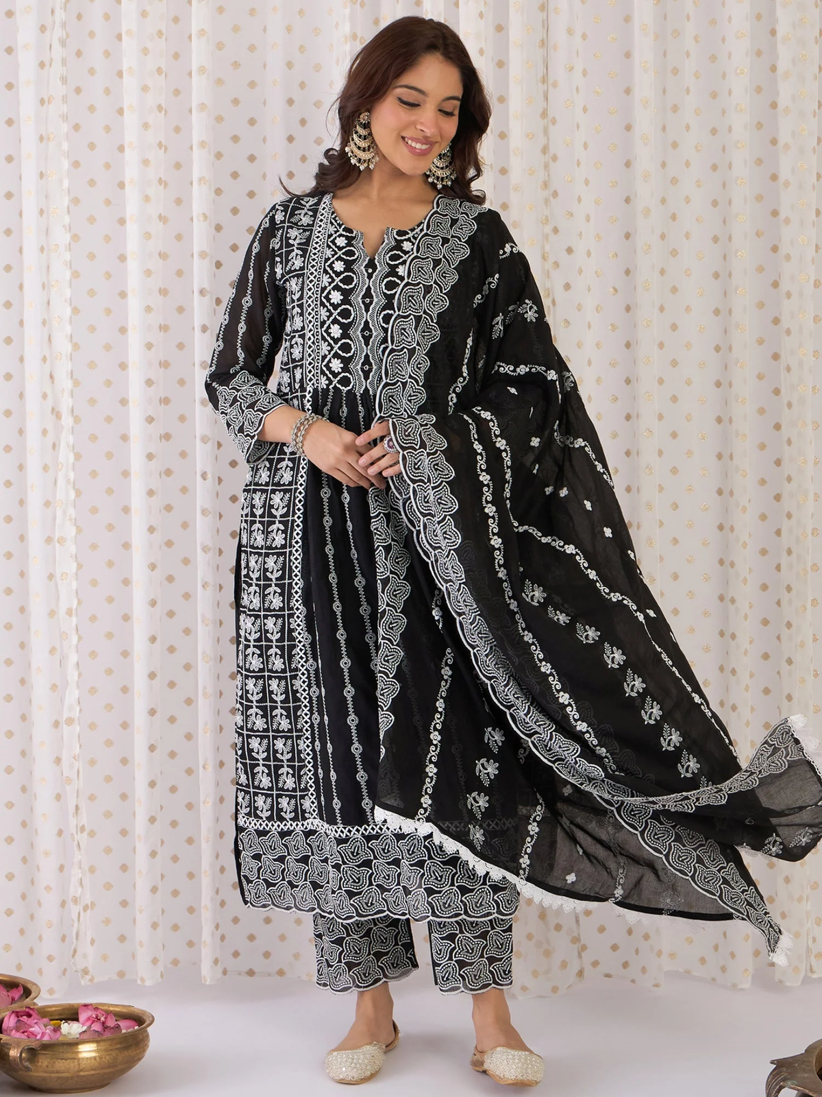 Woman wearing a black and white embroidered traditional outfit against a white curtain background