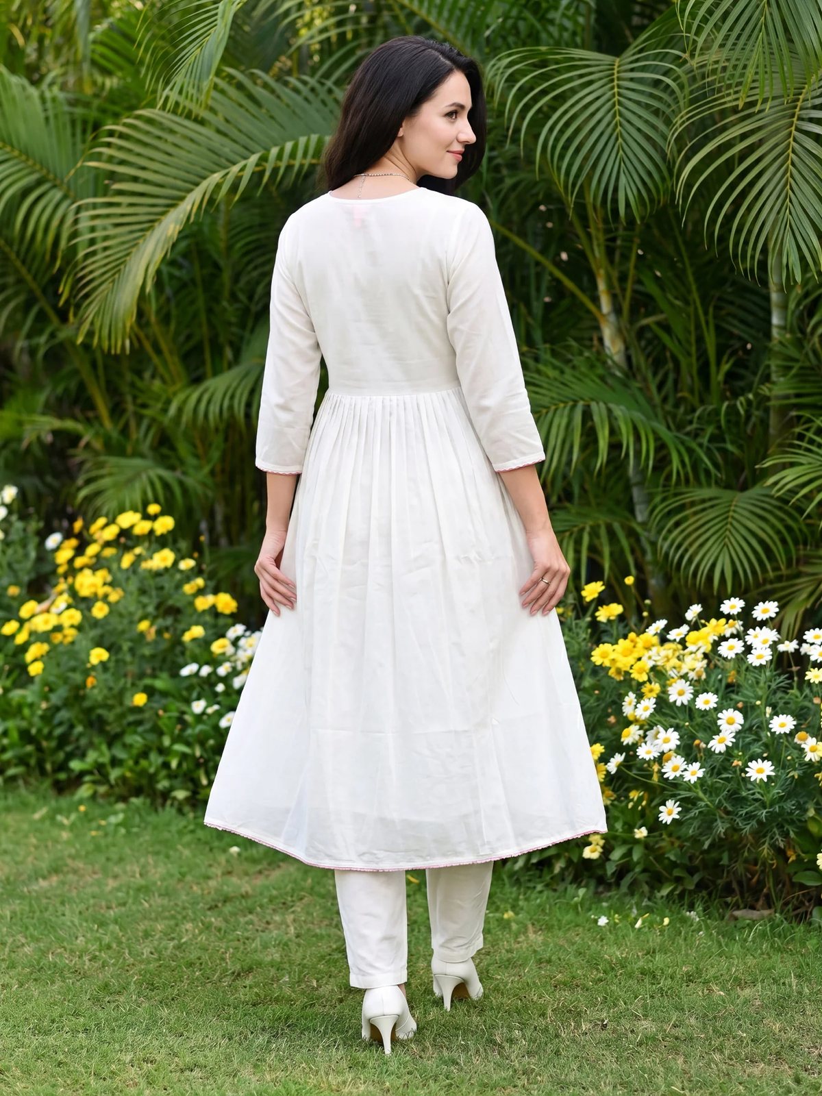Woman in a white dress standing in a garden with greenery and flowers.