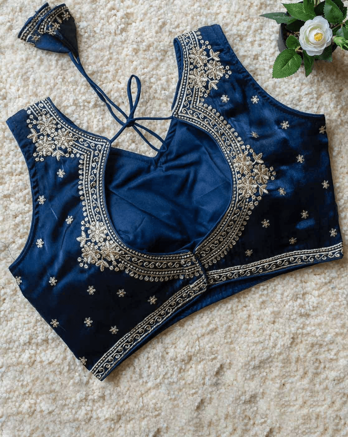 A navy blue velvet blouse top with intricate gold embroidery and star motifs, laid flat on a beige textured rug with a small white flower in the corner.