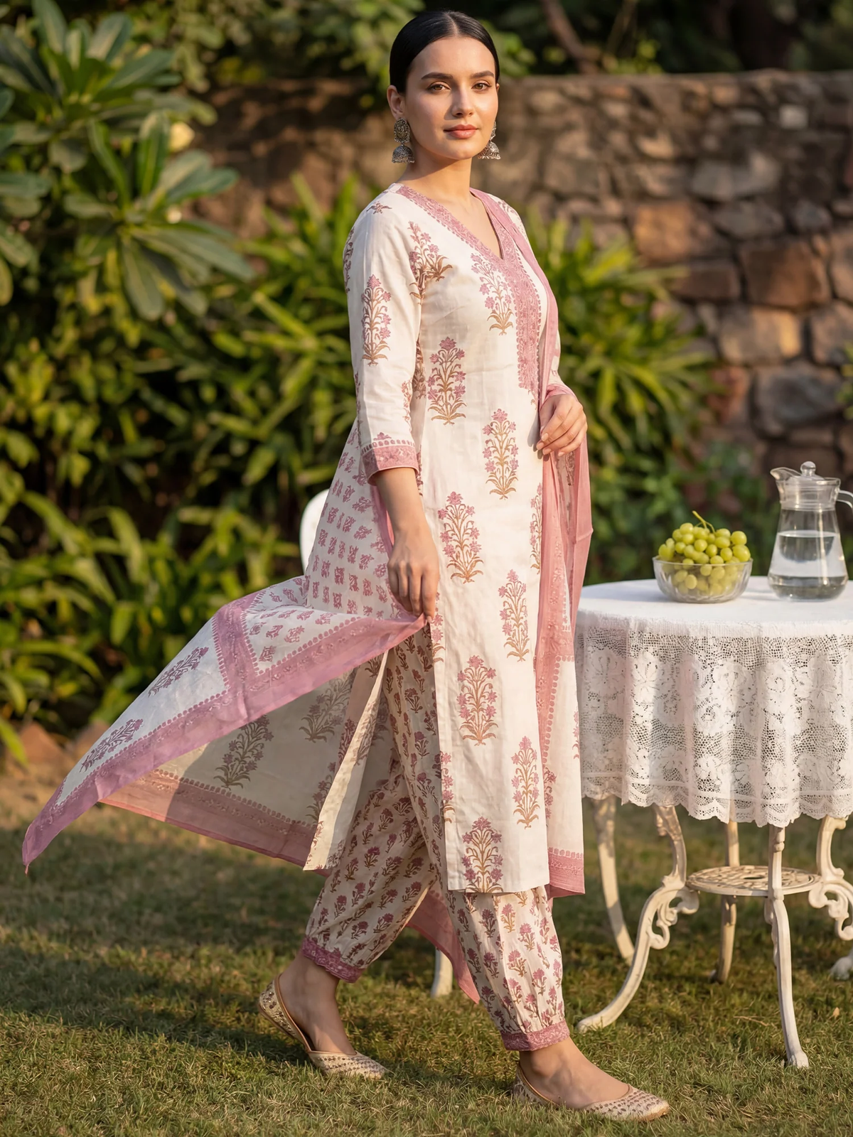 Woman in a traditional outfit standing outdoors with a table and plants in the background