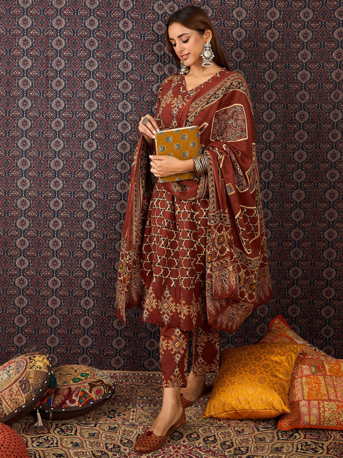 Woman in traditional maroon and gold embroidered outfit standing against a patterned wall.
