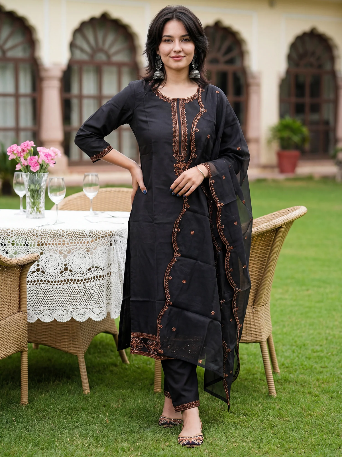 Woman in a black traditional outfit standing outdoors with a table and chairs in the background.