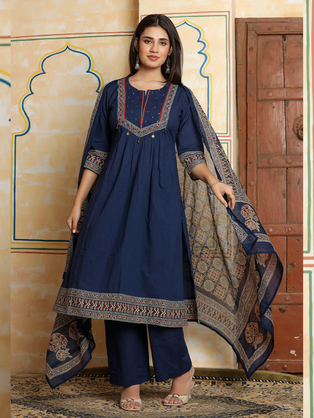 Woman wearing a navy blue traditional outfit with intricate patterns in a decorative setting.