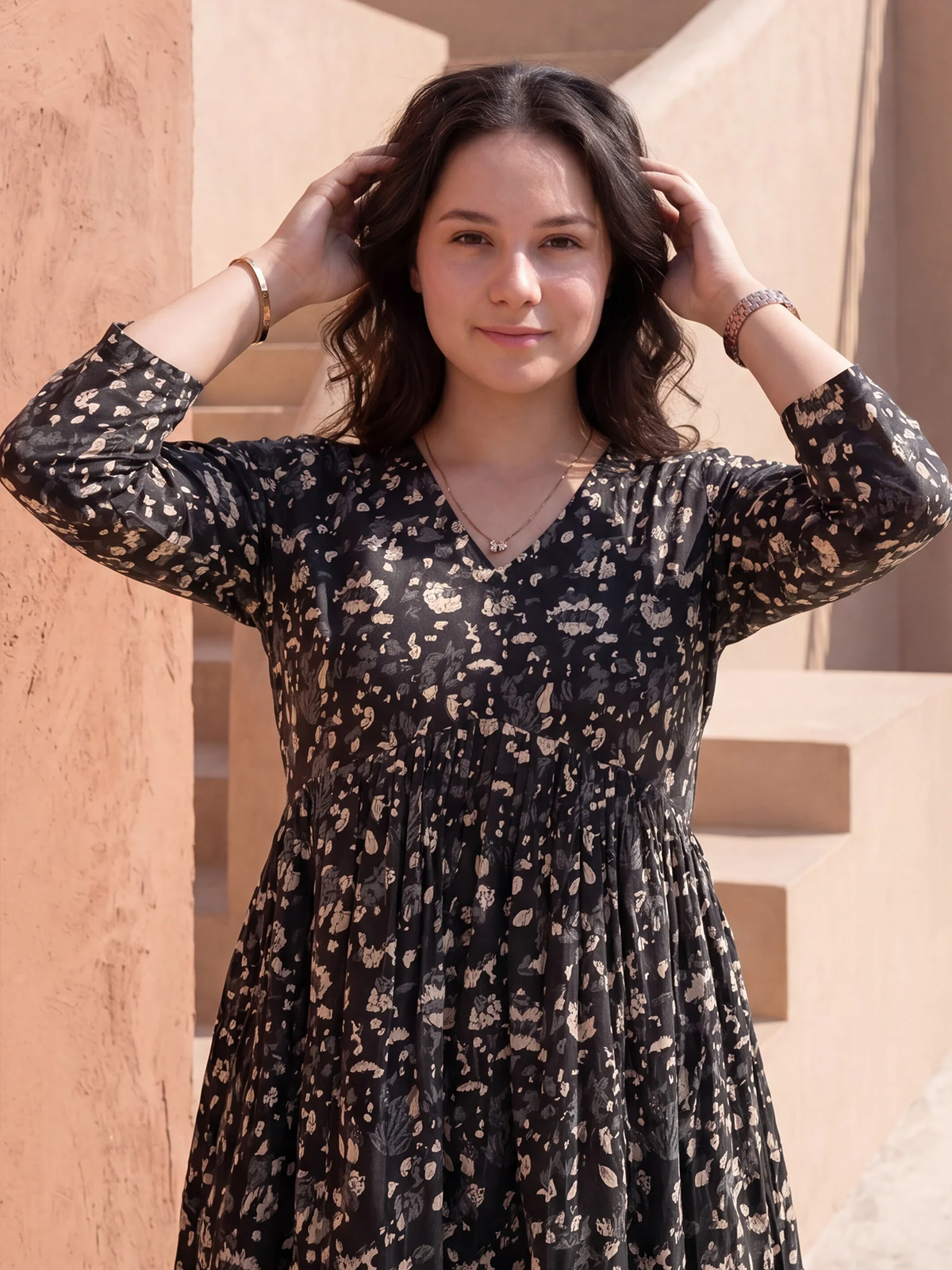 Woman wearing a black dress with a pattern, standing against a beige wall.