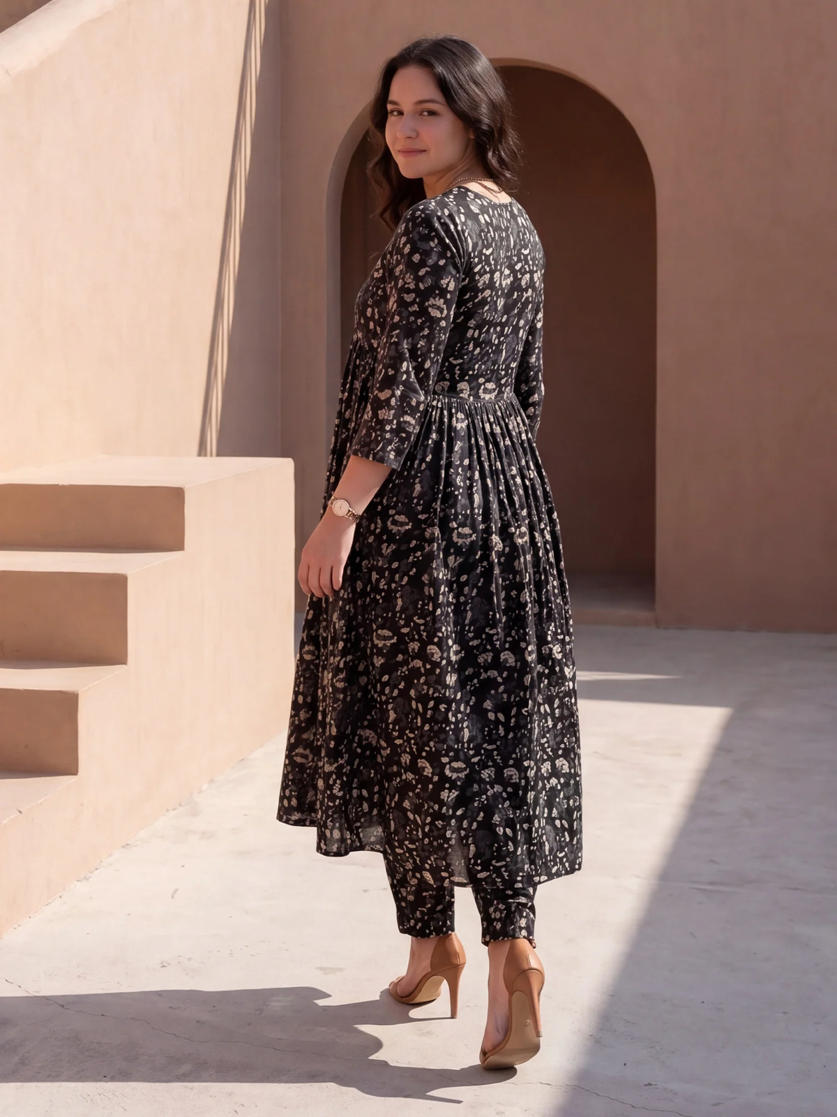 Woman in a black floral dress standing in front of a beige wall with arches.