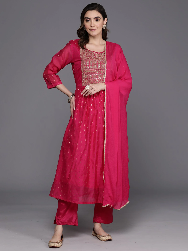 A woman modeling a bright pink traditional Indian outfit consisting of a kurta with embroidered neckline, matching pants, and a sheer dupatta, photographed against a solid gray studio background.