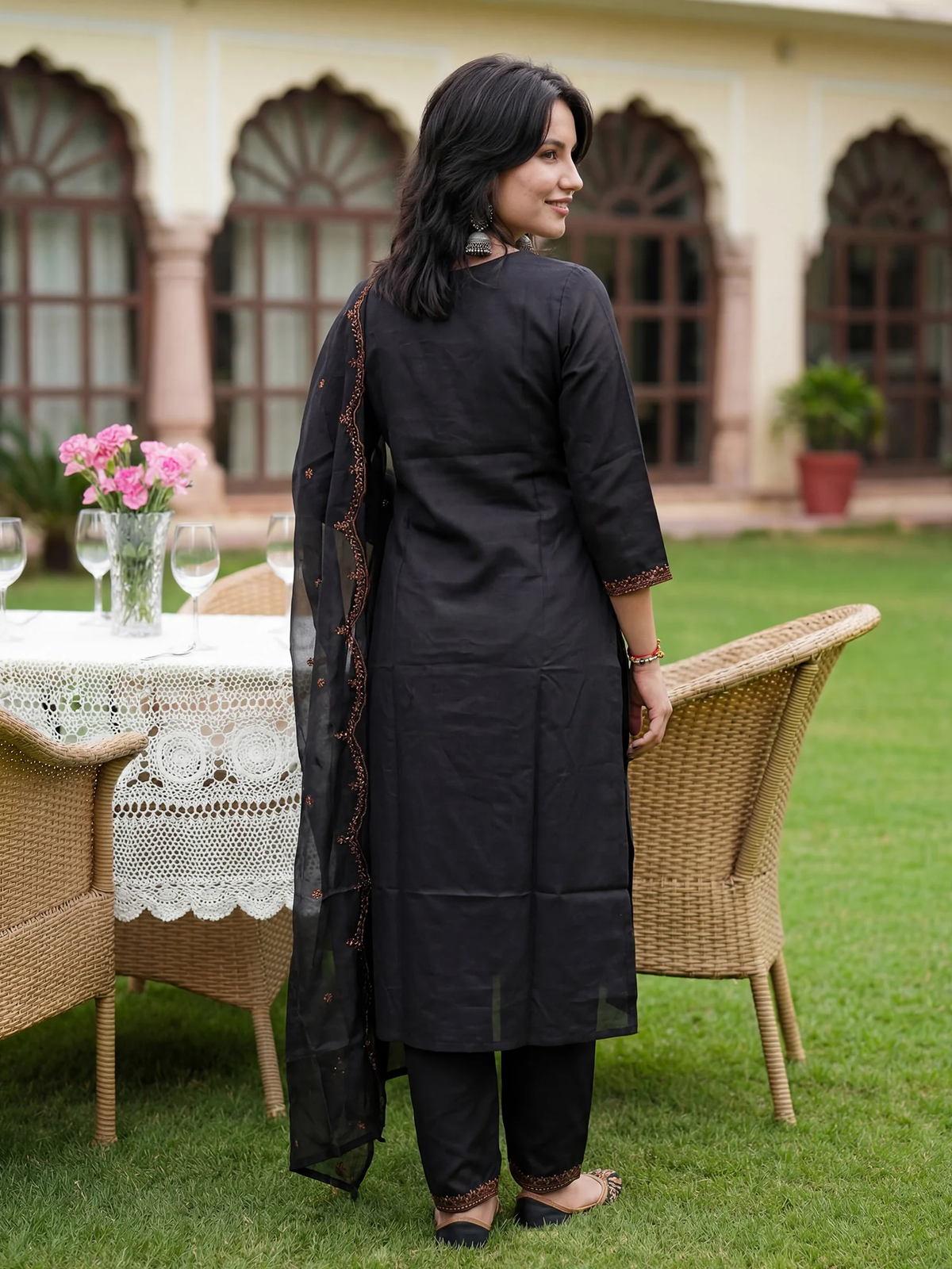 Woman in black traditional outfit standing outdoors with a table and chairs in the background