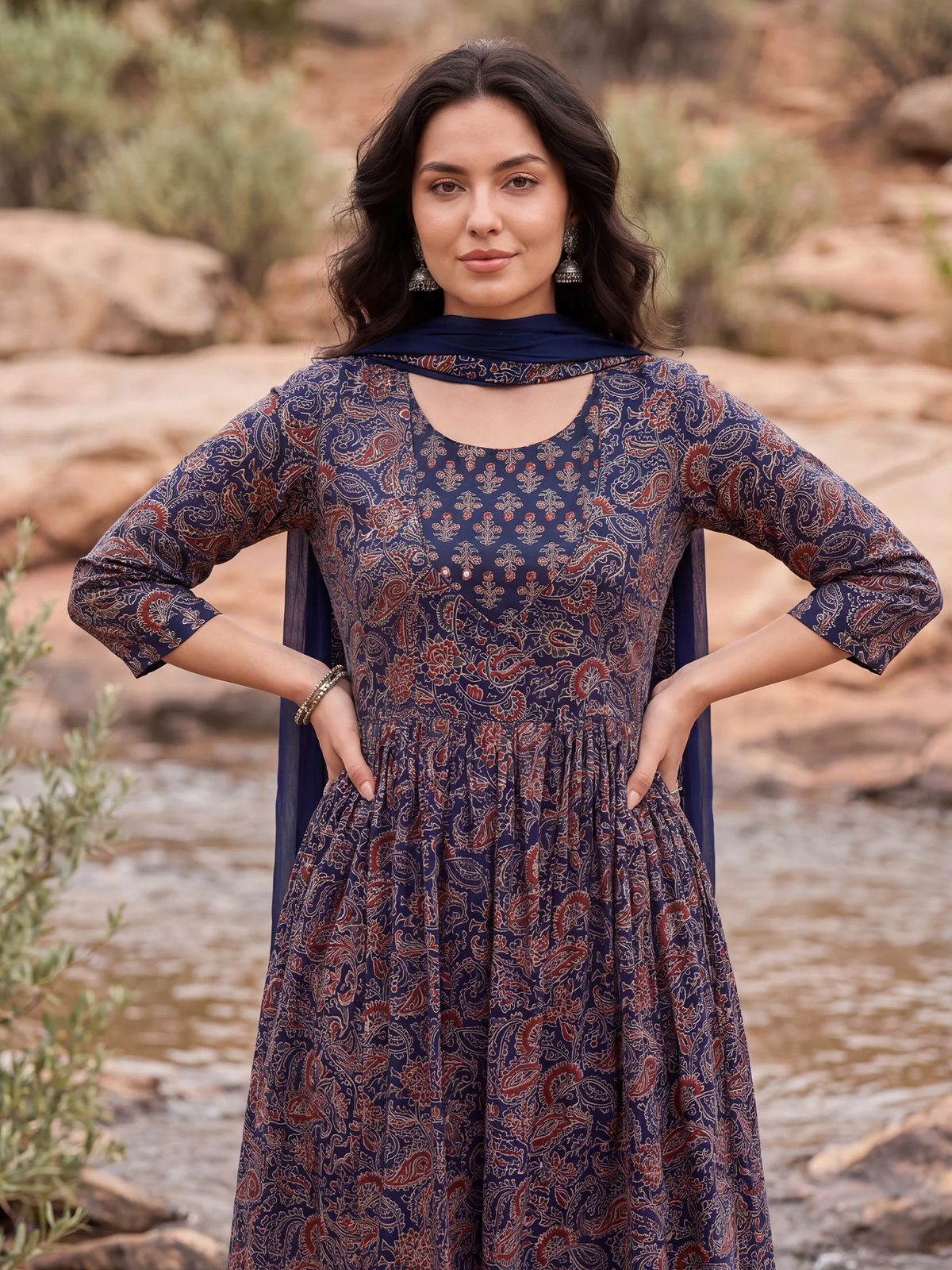 Woman wearing a patterned dress standing in a natural setting with rocks and plants.