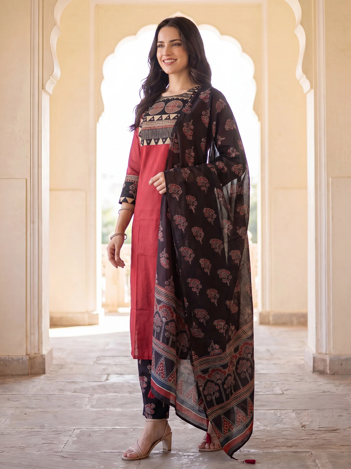 Woman wearing a traditional outfit with a pink and black design in an archway.