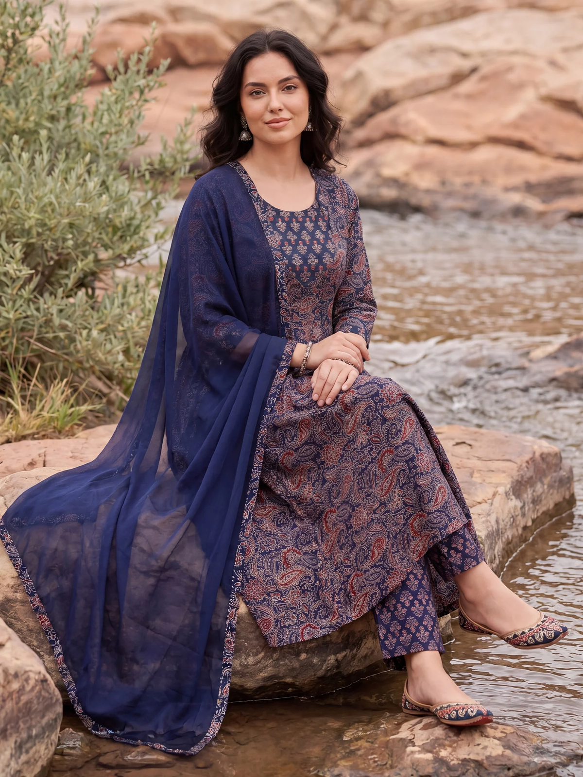 Woman in a traditional outfit sitting by a stream with a natural background