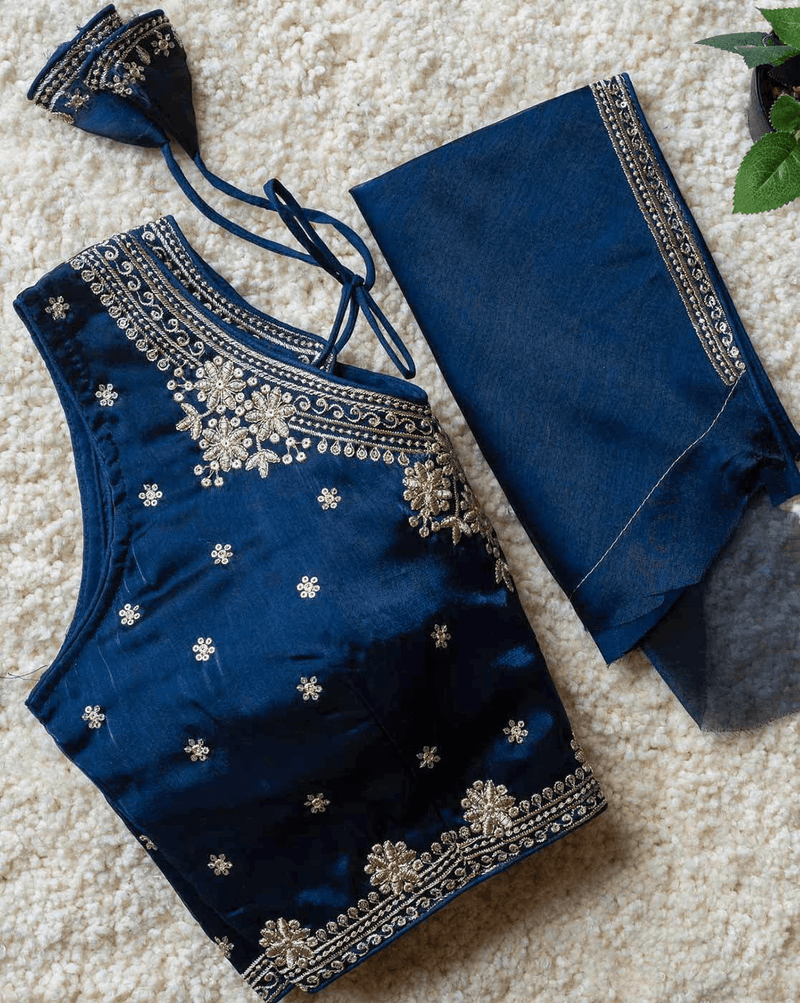 A dark blue traditional Indian outfit set, including a sleeveless embroidered blouse top with matching tie-neck strings and a pair of matching pants, laid flat on a beige textured rug.
