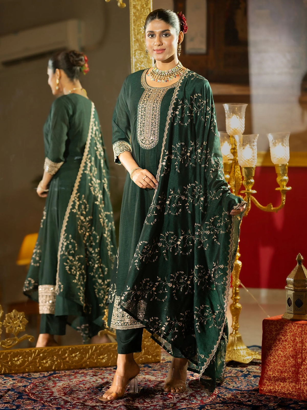 Woman in a green embroidered traditional outfit standing in an ornate room.
