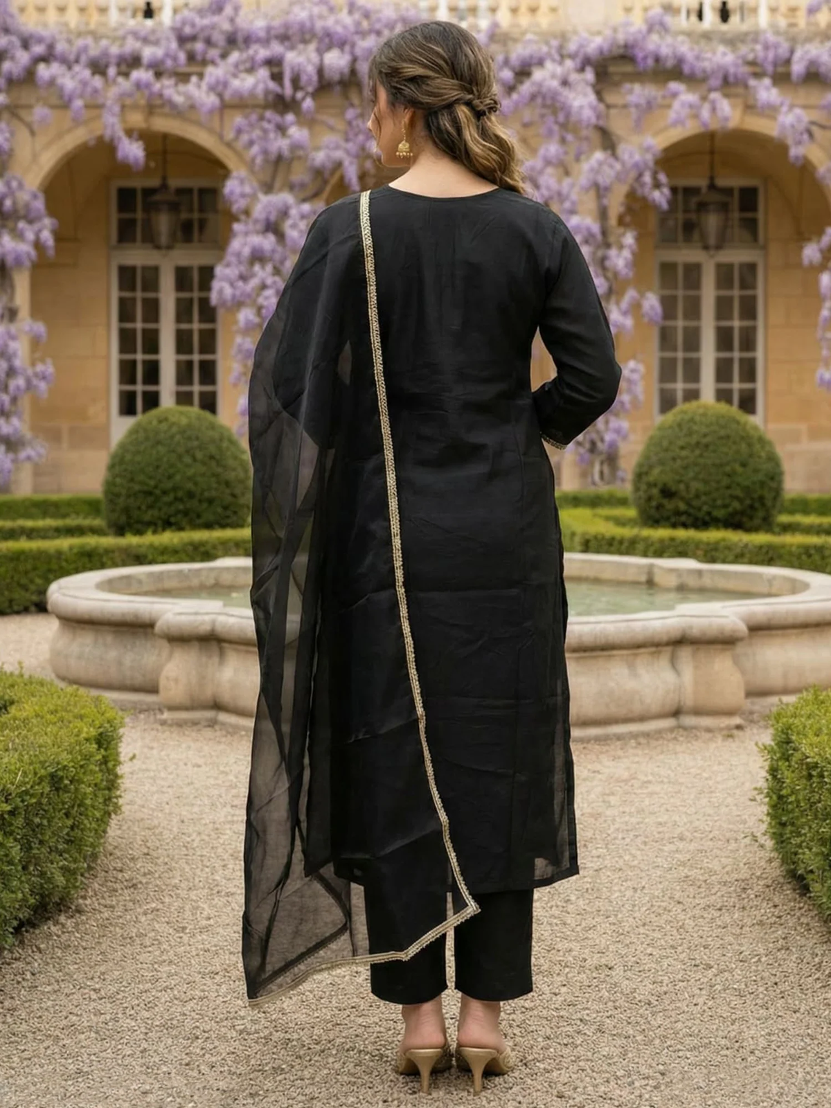Woman in a black outfit standing in a garden with floral decorations.