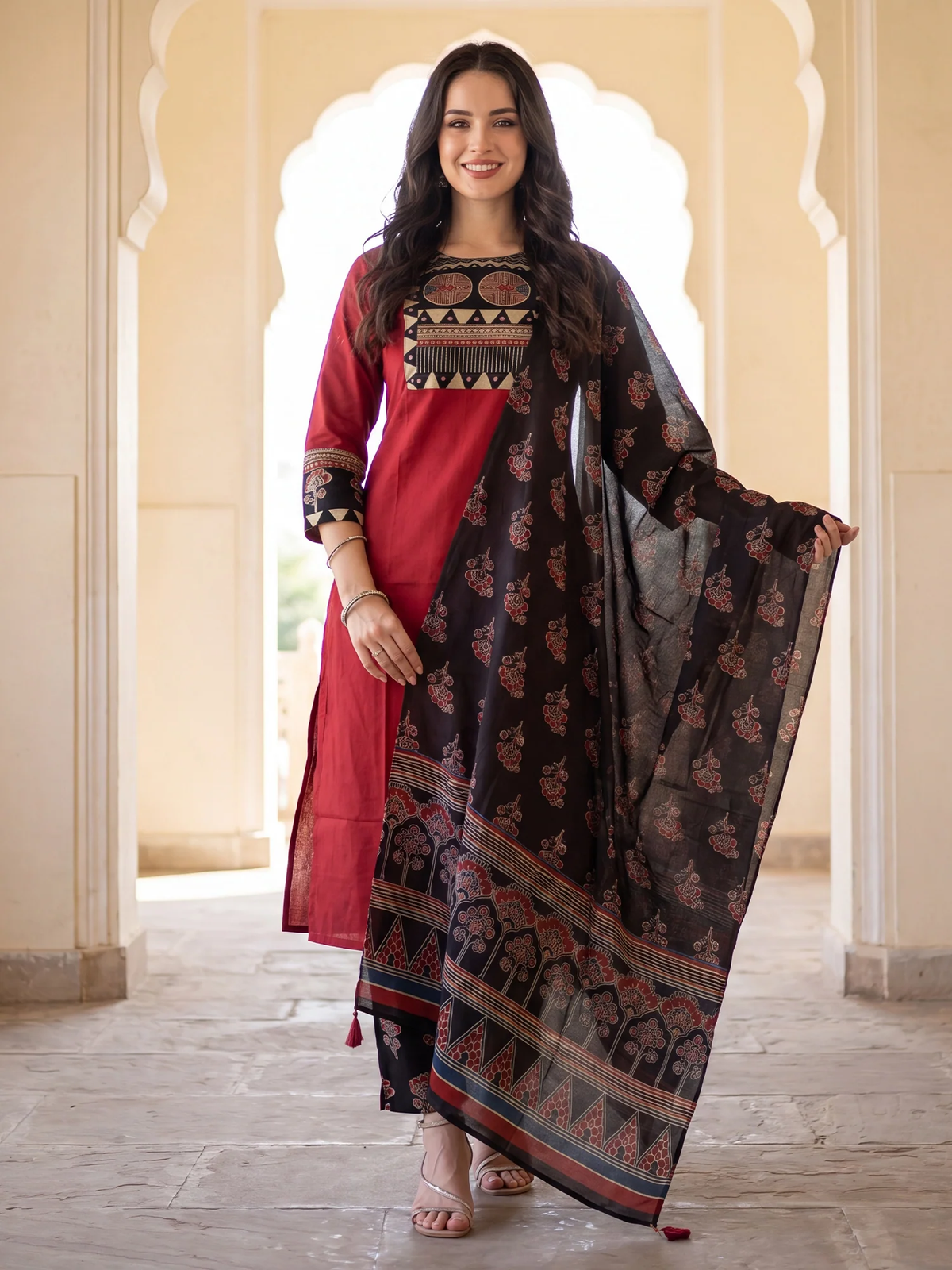 Woman wearing a red and black traditional outfit with a patterned dupatta in an elegant setting.