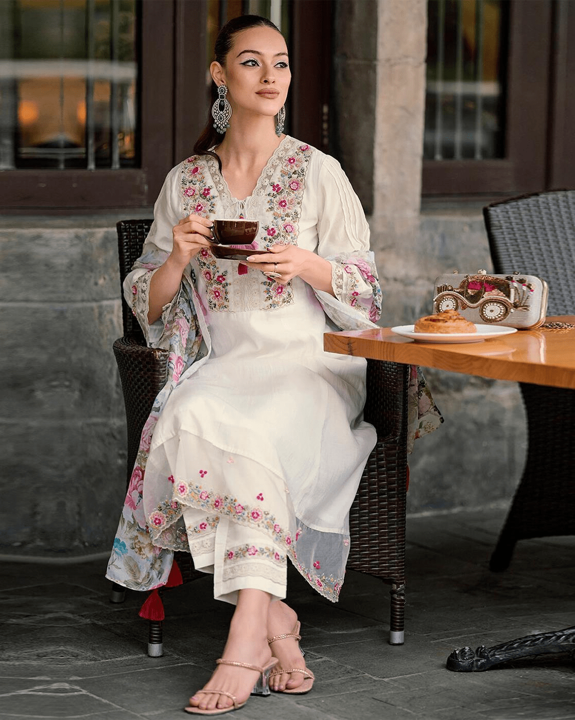 Elegant woman wearing an embroidered cotton kurta set, sipping tea at a café with floral details