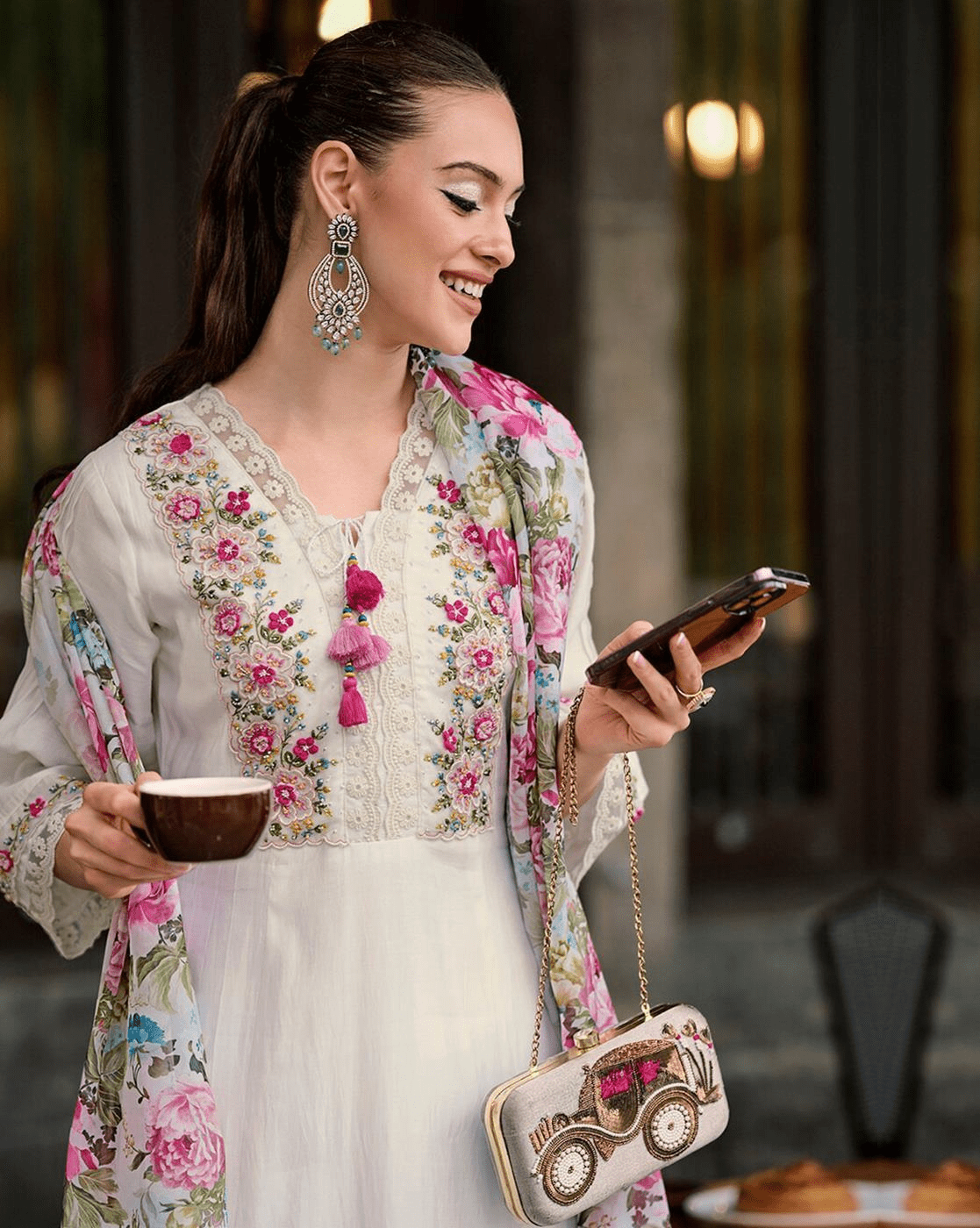 Elegant woman in an embroidered cotton kurta set, enjoying coffee while using her phone