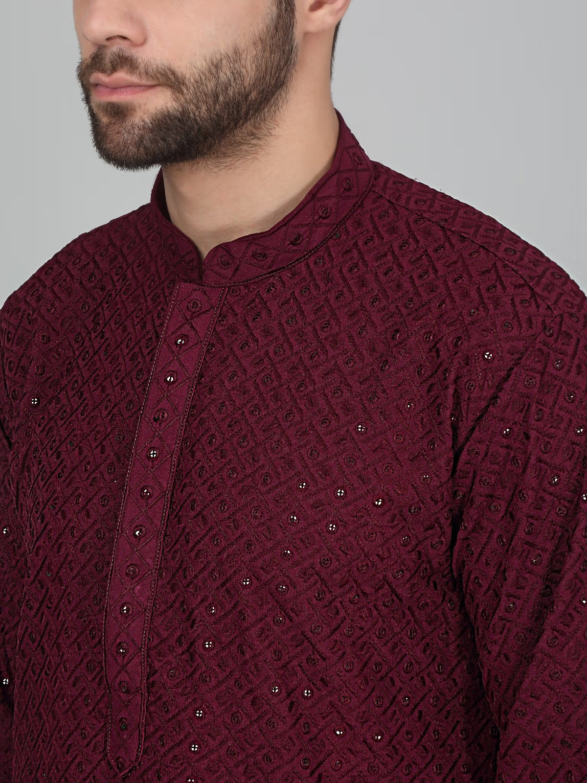 Close up of model wearing men's burgundy embroidered kurta set with mandarin collar textured diamond embroidery and button placket