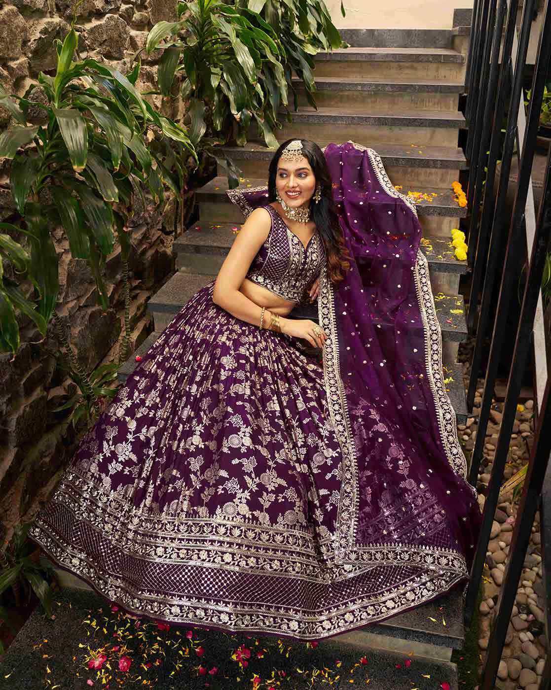Model wearing a purple embroidered lehenga choli set Canada with heavy silver embroidery and matching dupatta on stone steps