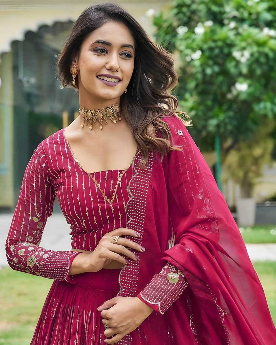 Smiling woman in magenta embroidered lehenga choli set Canada with gold choker jewelry long sleeves and dupatta