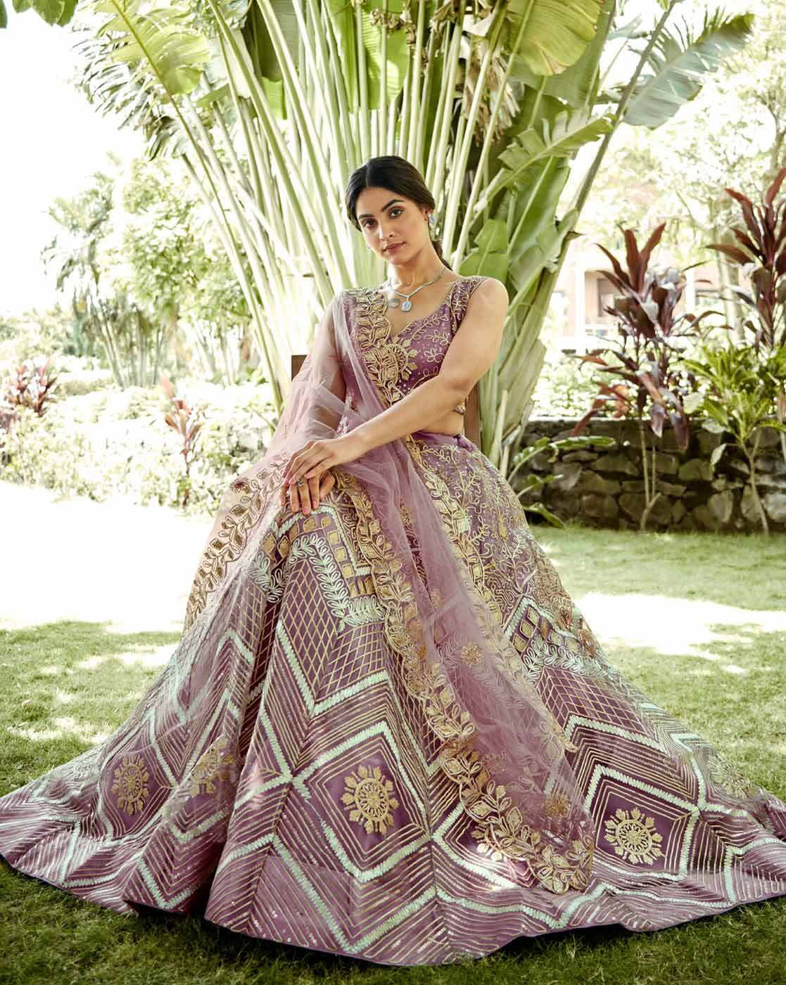 Woman wearing a mauve embroidered lehenga choli set Canada with gold floral embroidery and sheer dupatta seated outdoors