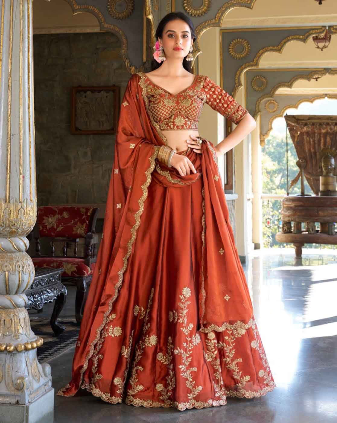 Model wearing rust orange embroidered lehenga choli set Canada with gold floral embroidery matching dupatta and blouse