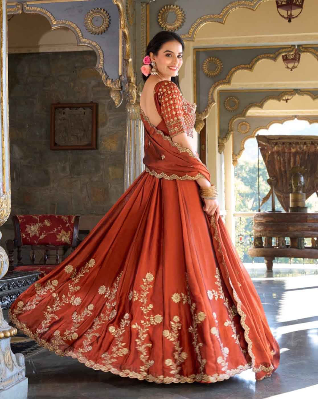 Woman in rust orange embroidered lehenga choli set Canada with gold floral embroidery and backless choli in ornate Indian palace
