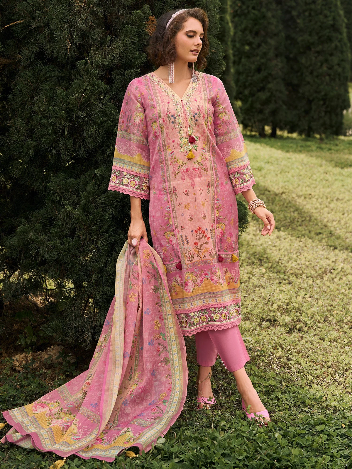 Woman wearing a pink embroidered traditional outfit with a matching dupatta outdoors.