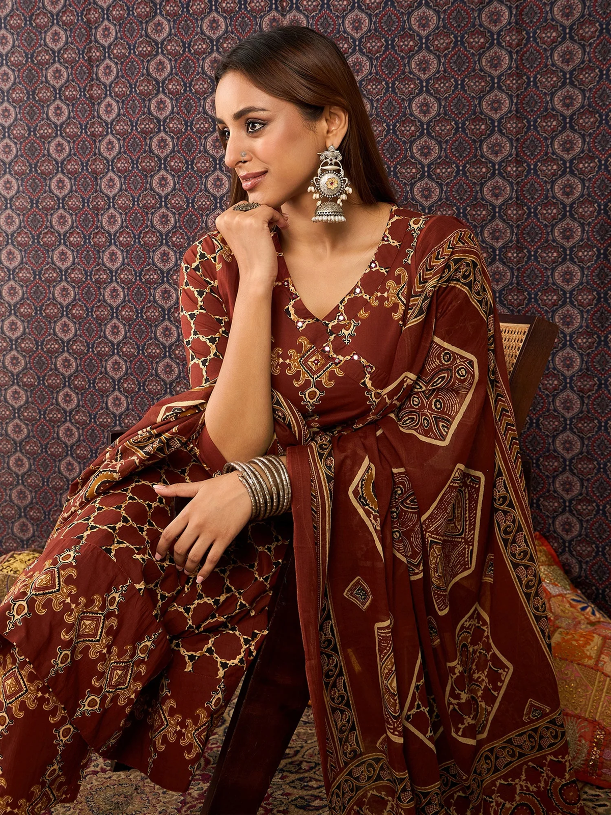 Woman wearing a patterned red and gold traditional outfit against a decorative wall.
