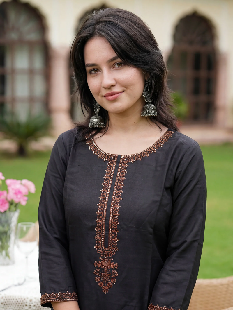 Woman wearing a black embroidered dress outdoors with blurred background