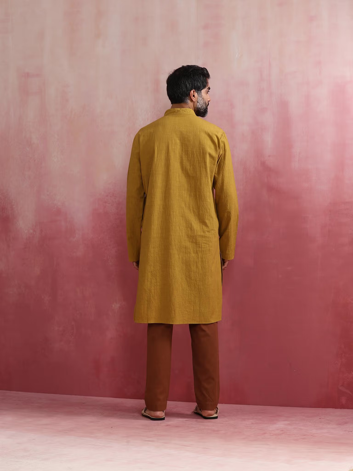 Rear view of model wearing men's mustard kurta Canada with brown pants against pink backdrop