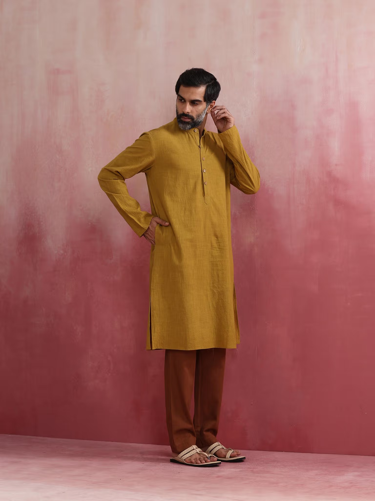 Male model wearing men's mustard kurta Canada with brown pants and sandals against pink backdrop