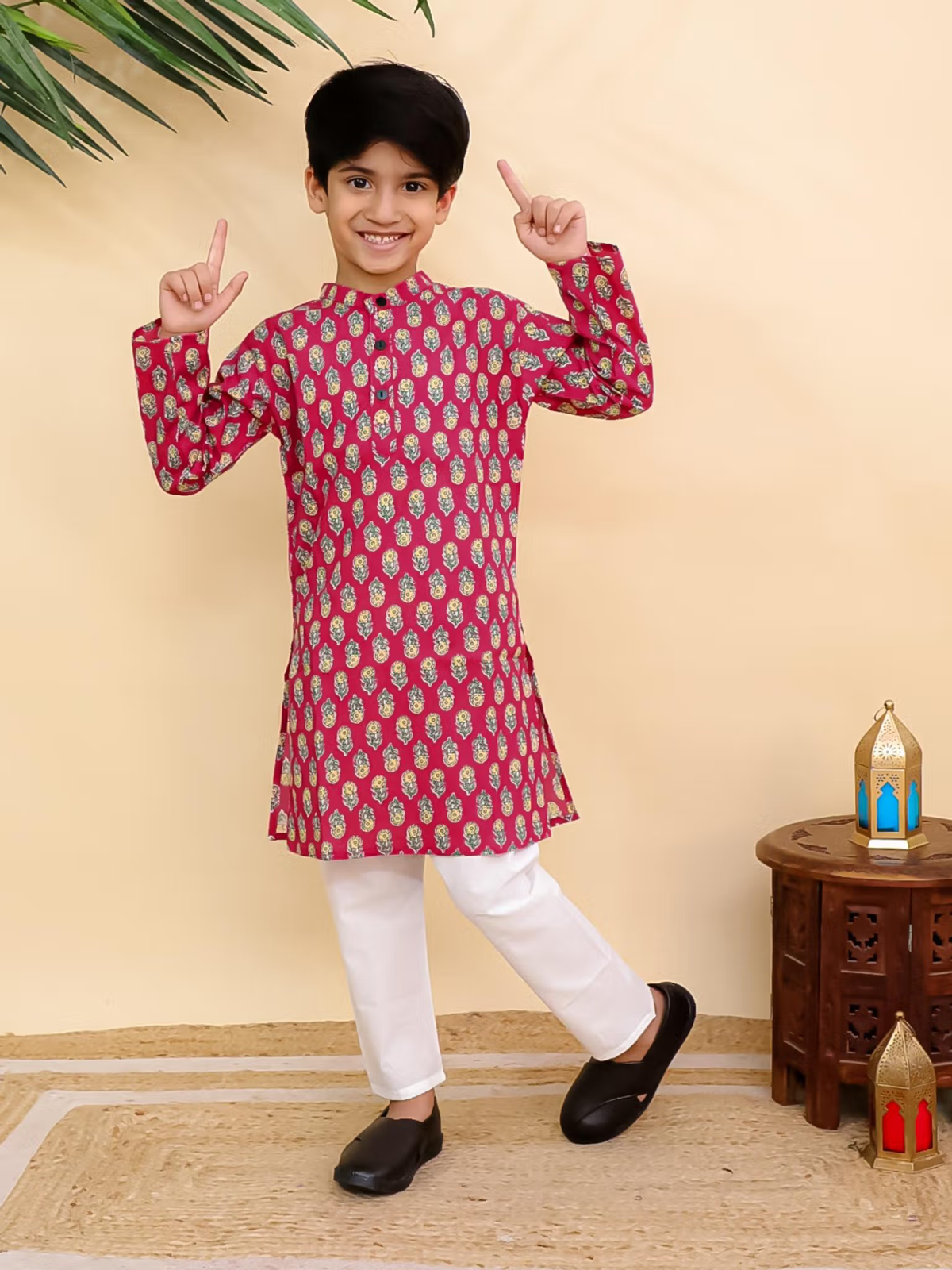 Smiling boy wearing red printed kurta pyjama set Canada with white pants black shoes pointing up in studio