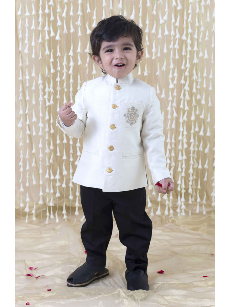 Smiling toddler in cream bandhgala for baby boys with gold buttons and embroidery paired with black pants for festive occasions