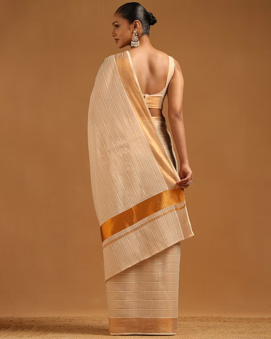 Back view of a cream-colored saree with golden stripes, ideal for weddings, made from lightweight fabric