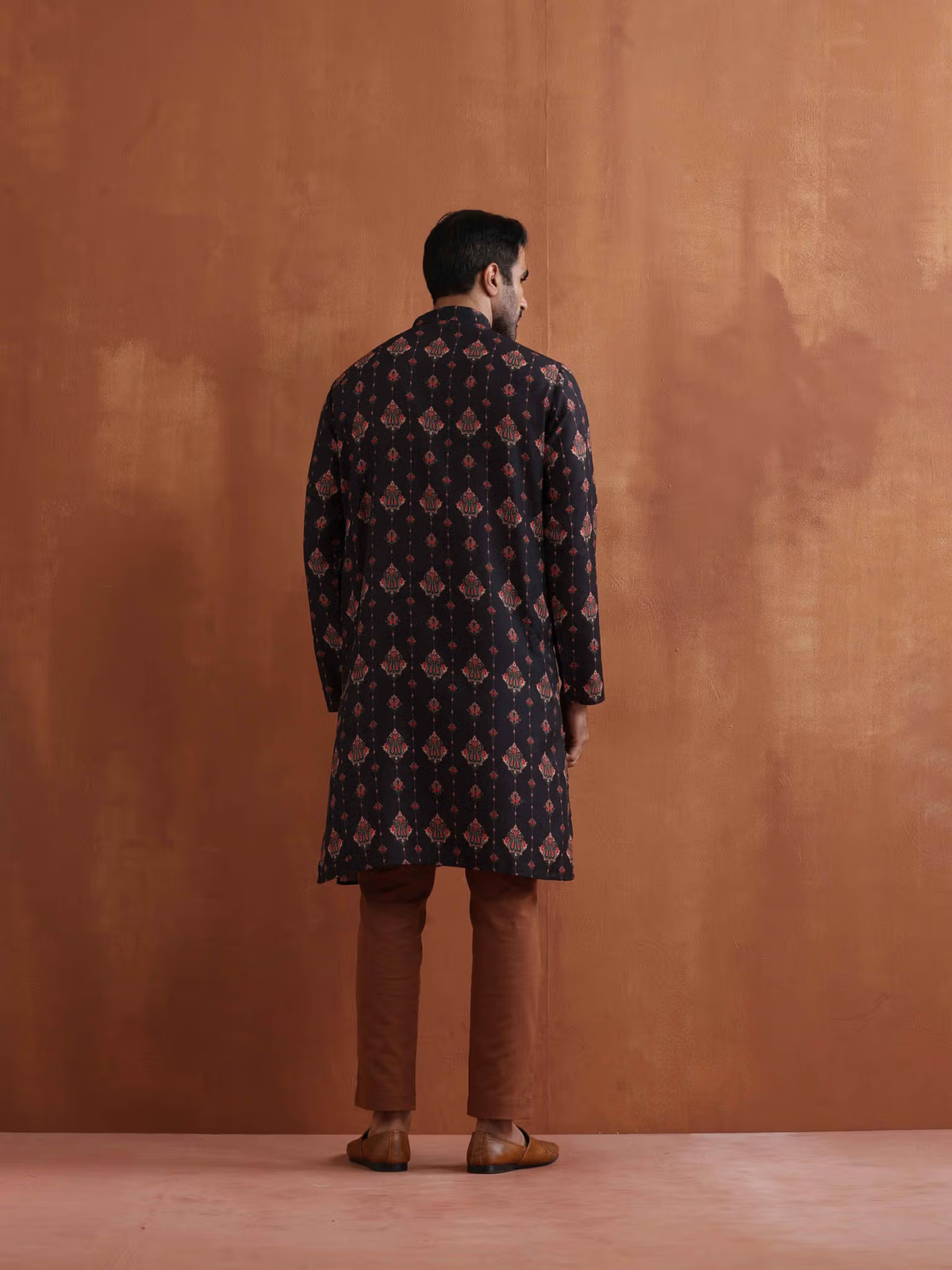 Rear view of model wearing AROMIE men's black printed kurta with geometric motifs brown pants and leather shoes