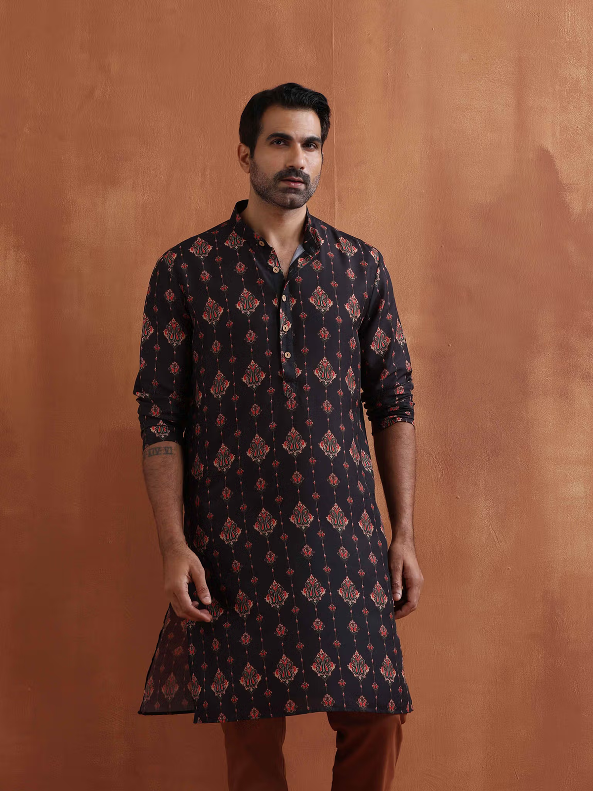 Model wearing men's black printed kurta with red geometric motifs and mandarin collar paired with brown trousers