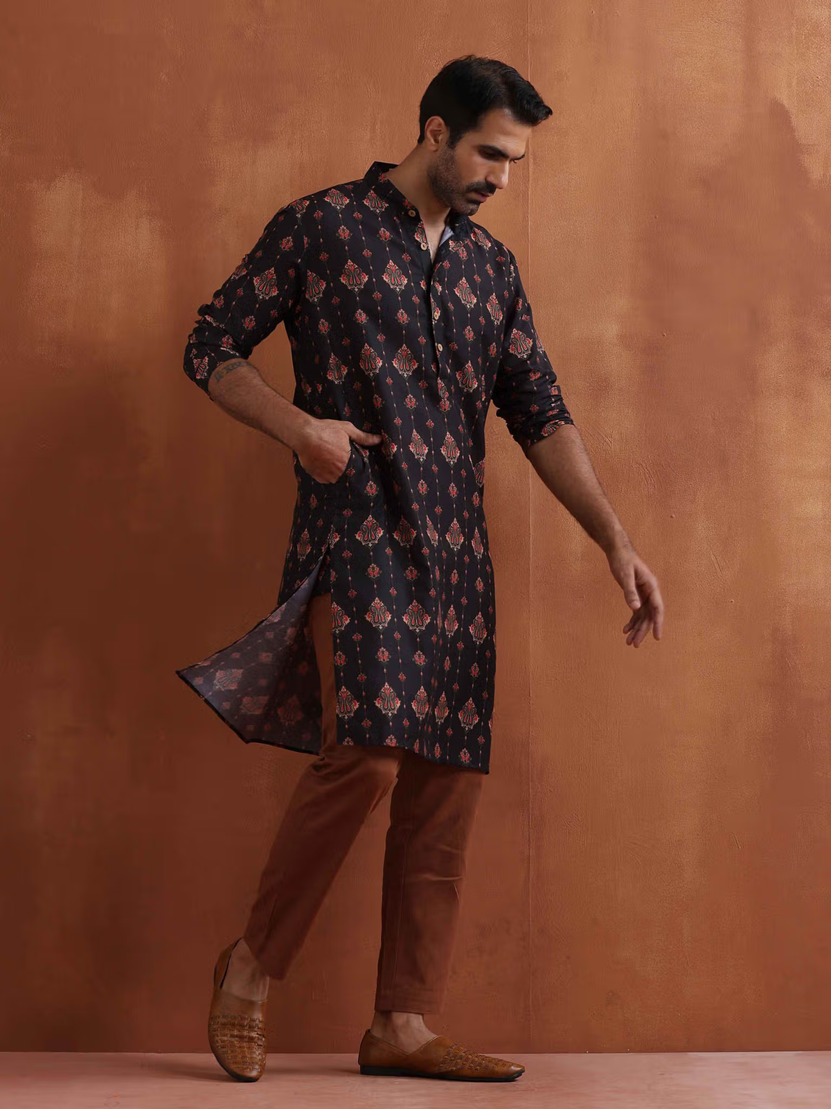 Model wearing men's black printed kurta with long sleeves high side slits and brown trousers