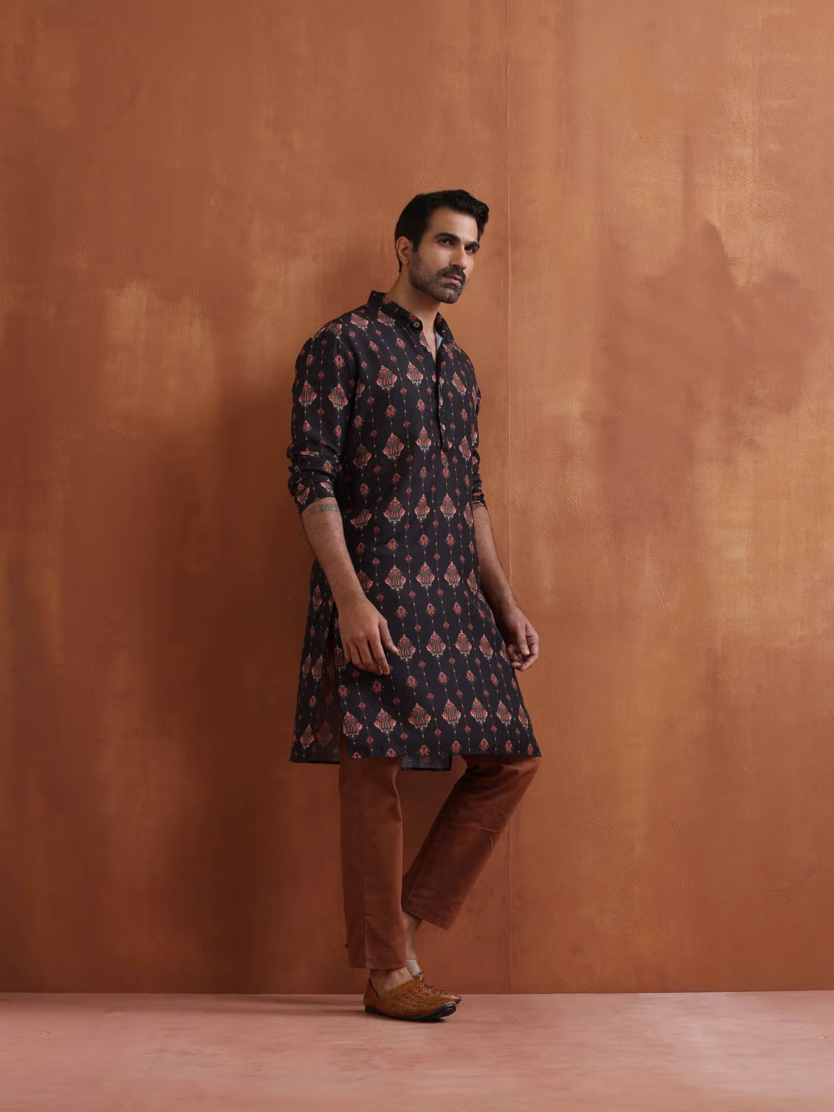 Male model wearing men's black printed kurta with ethnic red motifs, brown pants and leather shoes