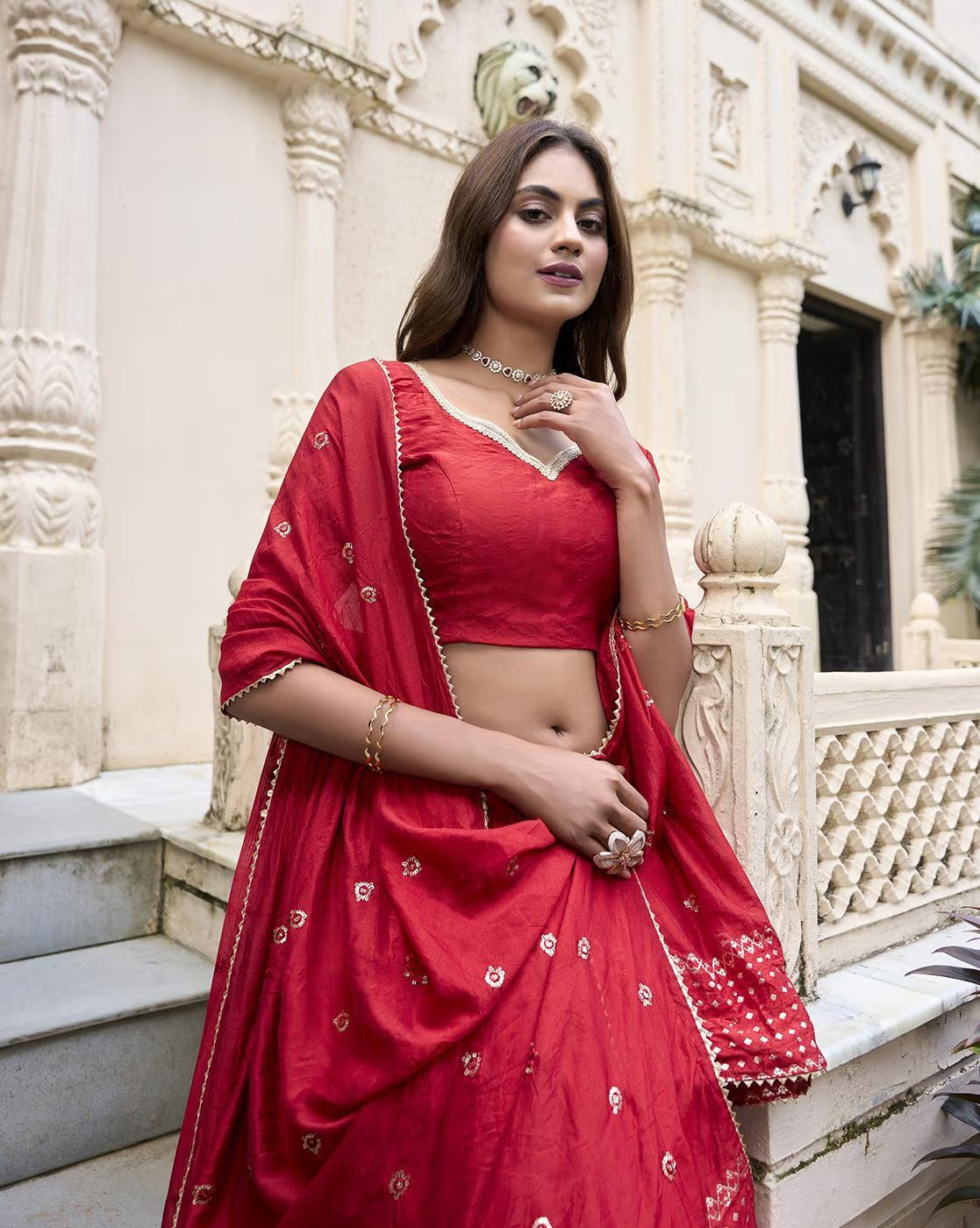 Red embroidered lehenga choli set with gold motifs and matching dupatta worn by model at ornate heritage venue