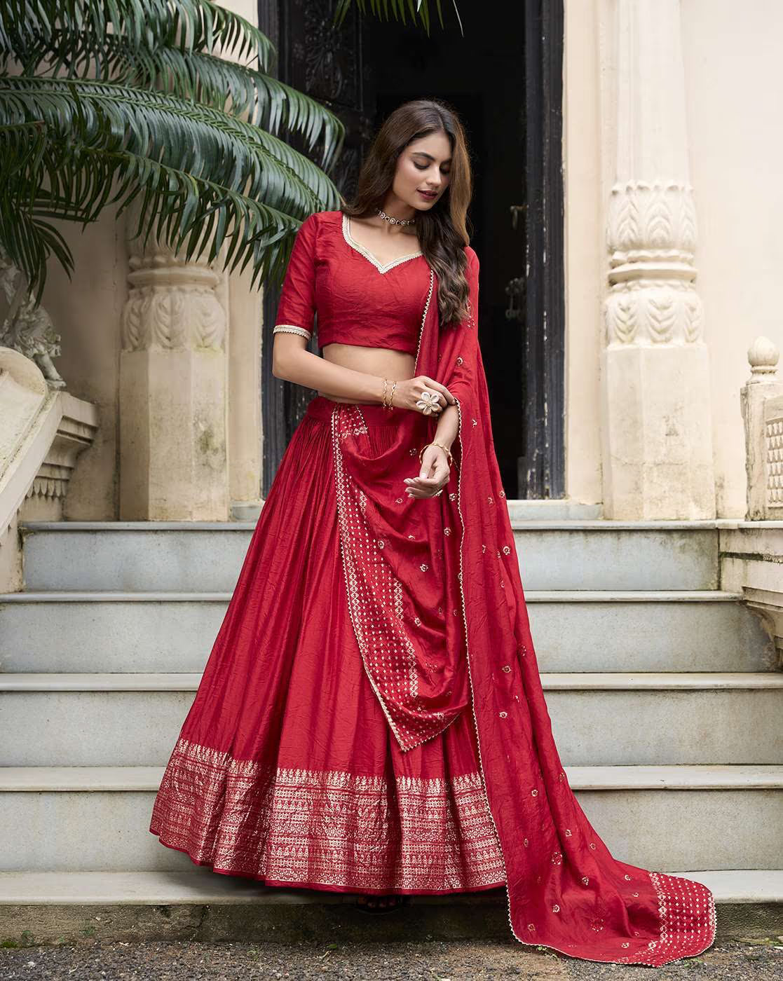 Woman wearing red embroidered lehenga choli set with gold border and matching dupatta on stone steps