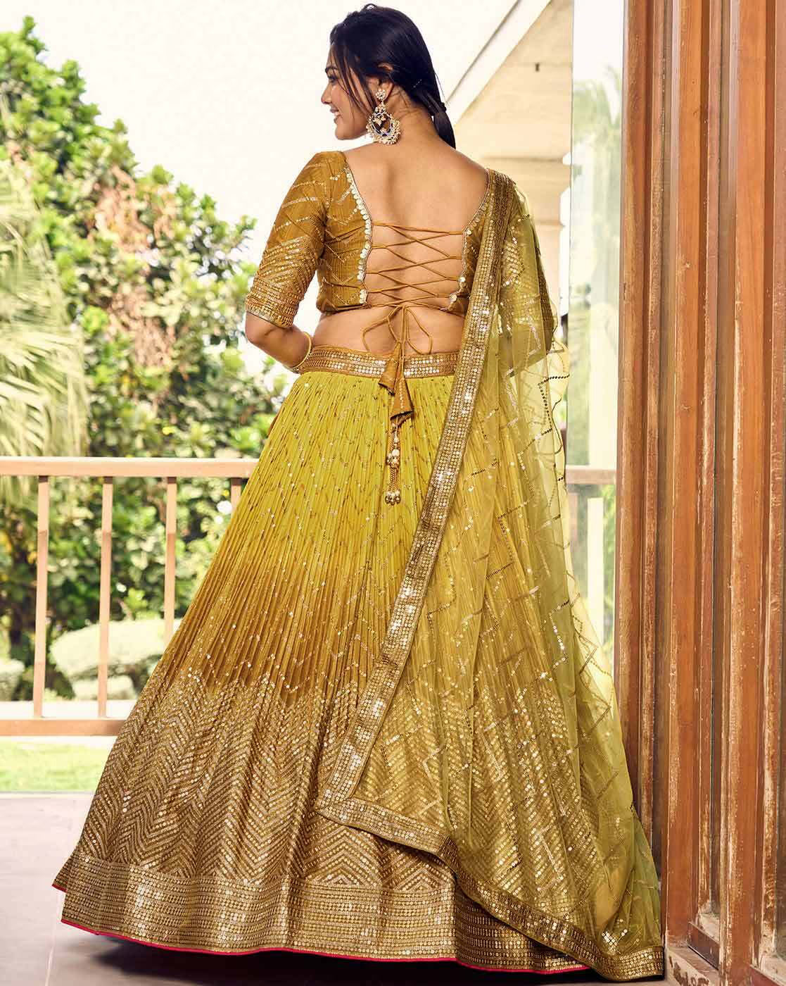 Back view of model in gold embellished flared lehenga choli Canada with lace up blouse and sheer dupatta