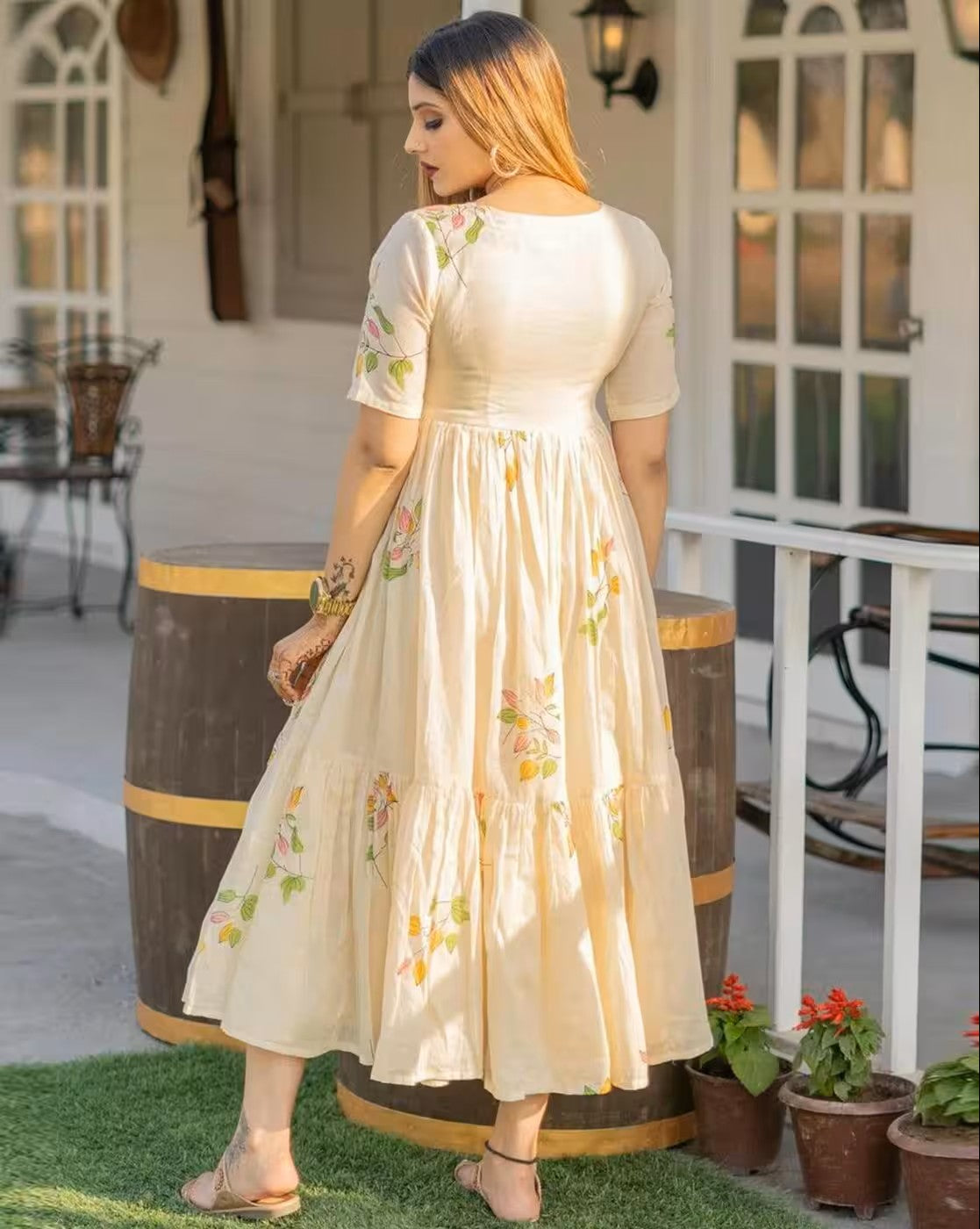 Woman wearing aromie rust orange mini dress with floral patterns standing outdoors near barrels and plants