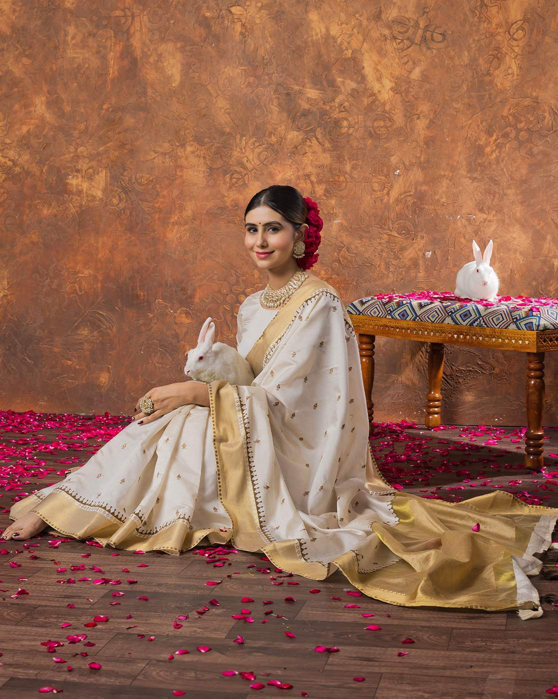 Aromie sequin embellished saree online in white and gold with intricate border worn by a woman holding a white rabbit