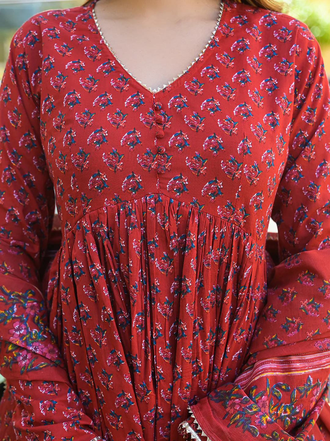 Close-up of red Anarkali kurta trouser set with dupatta featuring floral patterns and intricate detailing.