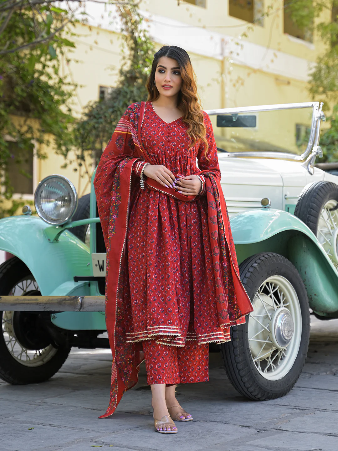 Elegant red Anarkali kurta trouser set with dupatta styled in a vintage outdoor setting