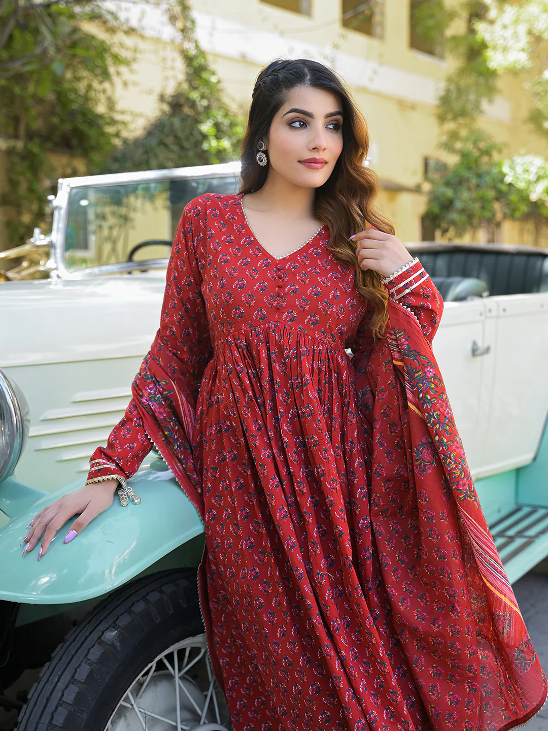 Model wearing a red Anarkali kurta trouser set with dupatta, styled elegantly outdoors